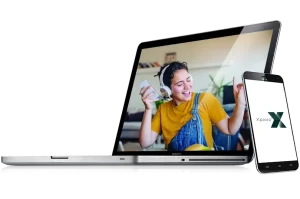 Laptop with image of girl listening to music on the screen with mobile phone leaning against laptop.