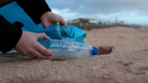 Man picking up a water bottle on a beach